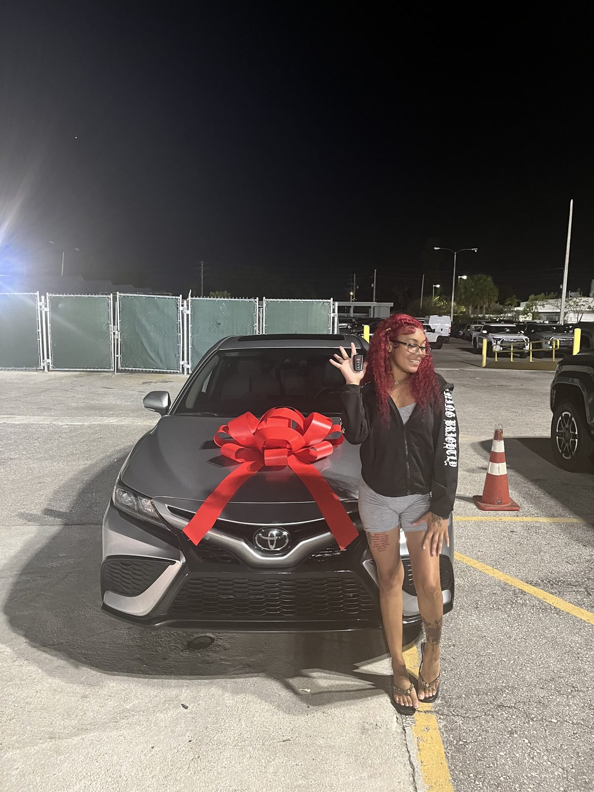 Customer posing beside a grey sedan with a red bow at night.